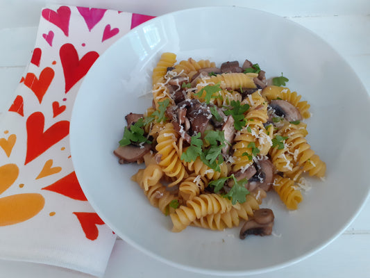 Garlicky mushroom pasta in a white pasta bowl with a rainbow hearts cloth napkin