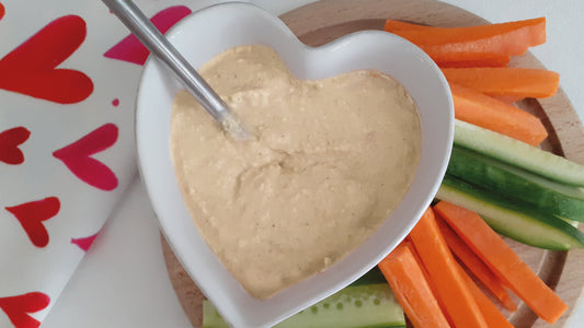 Humus in a pot with raw carrots, cucumber and cauliflower on a wooden board and a blue star tea towel