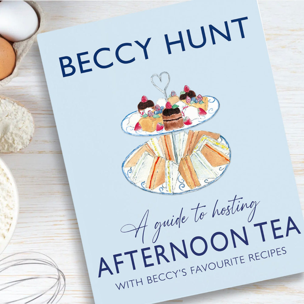 Cover of 'A Guide to Hosting Afternoon Tea' by Beccy Hunt, featuring recipes for traditional British afternoon tea. The book is displayed on a wooden surface with baking ingredients, including eggs, flour, and a whisk. Join the Baking Demonstration & Afternoon Tea event on Saturday, 10th May and 7th June, to learn scone baking and enjoy a classic tea experience.