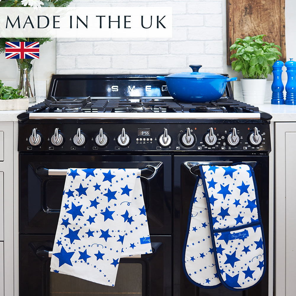 Blue Shooting Stars Tea Towel and matching Double Oven Glove hanging over a black range cooker, with blue dishes on top, featuring a hand-drawn blue and white star design