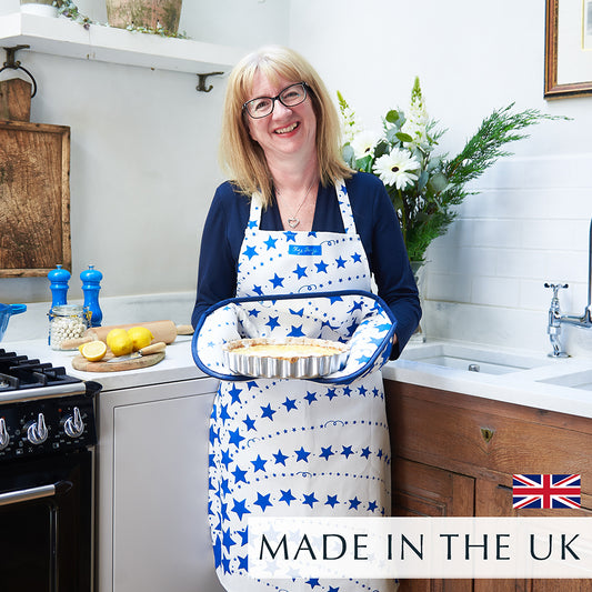 Beccy wearing the Blue Shooting Stars Apron in the kitchen, holding a freshly baked quiche, featuring a hand-drawn blue and white shooting star design