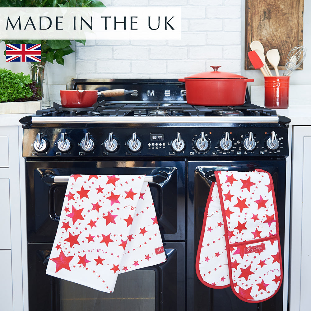 Red Shooting Stars Tea Towel and matching Double Oven Glove hanging over a black range cooker, with red dishes on top, featuring a hand-drawn shooting star design in bold red and white