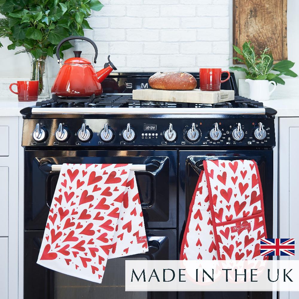 The bold red and white shooting heart design tea towel, hanging over a black range cooker next to the matching double oven glove.