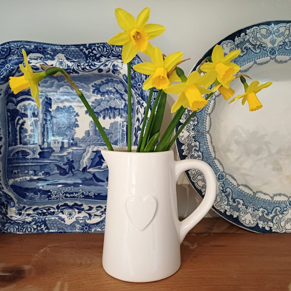 White pitcher with yellow daffodils in front of blue and white patterned plates