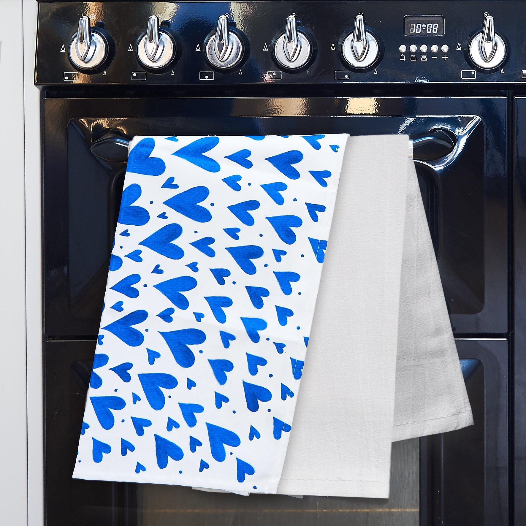 Blue heart tea towel and plain white tea towel hanging on a range cooker