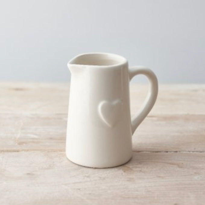 Elegant white ceramic milk jug with embossed heart design, featuring a curved handle and a small pouring spout. Perfect for serving cream, milk, or sauces at afternoon tea. Stylish farmhouse kitchen accessory. Ideal gift for tea lovers and home bakers.