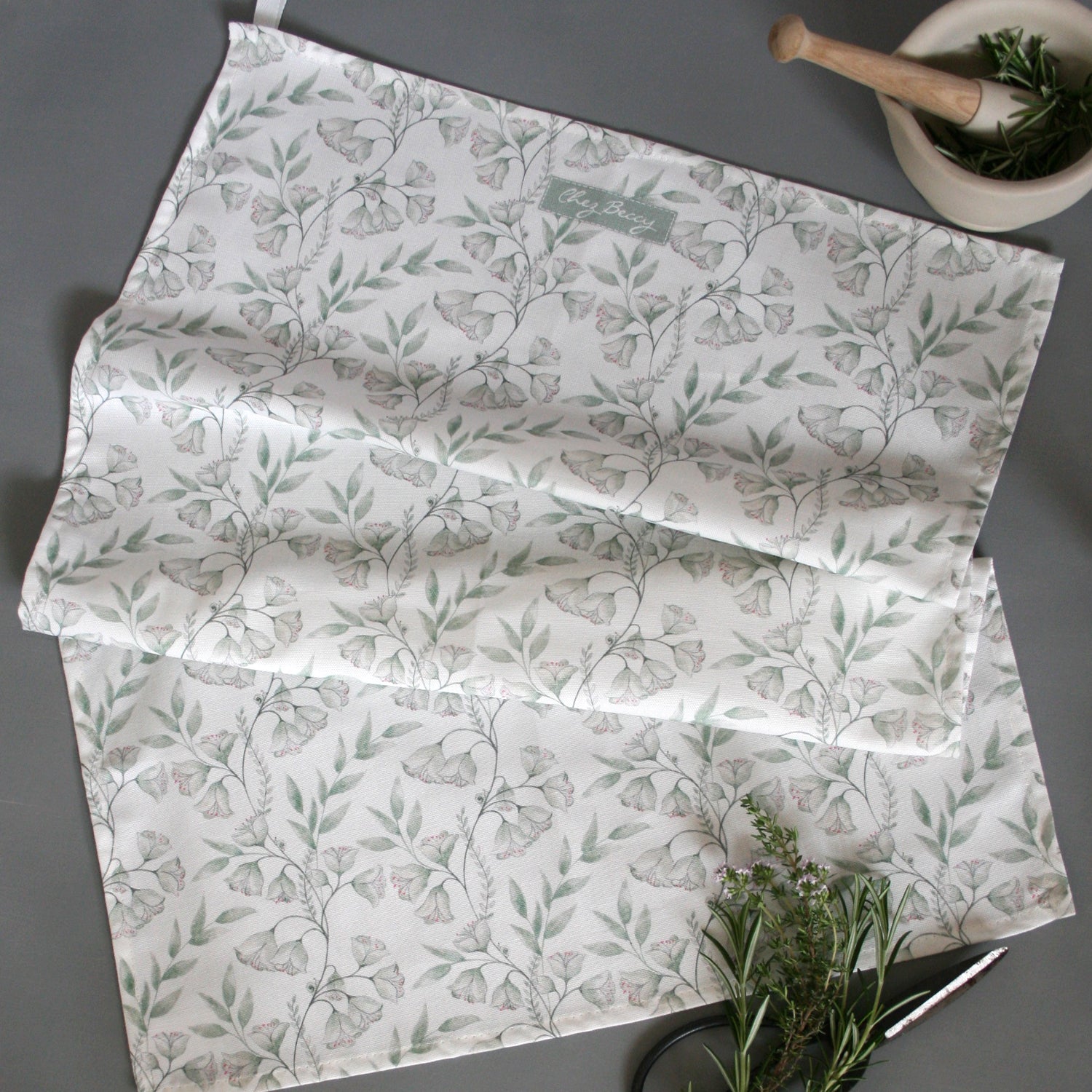 Sage green floral tea towel with an elegant clematis-inspired pattern, made from 100% cotton. Stylish, absorbent, and perfect for everyday kitchen use.