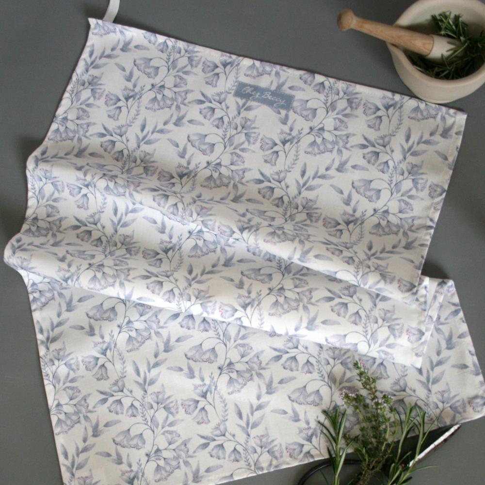 Grey floral tea towel with an elegant clematis-inspired pattern, made from 100% cotton. Stylish, absorbent, and perfect for everyday kitchen use.