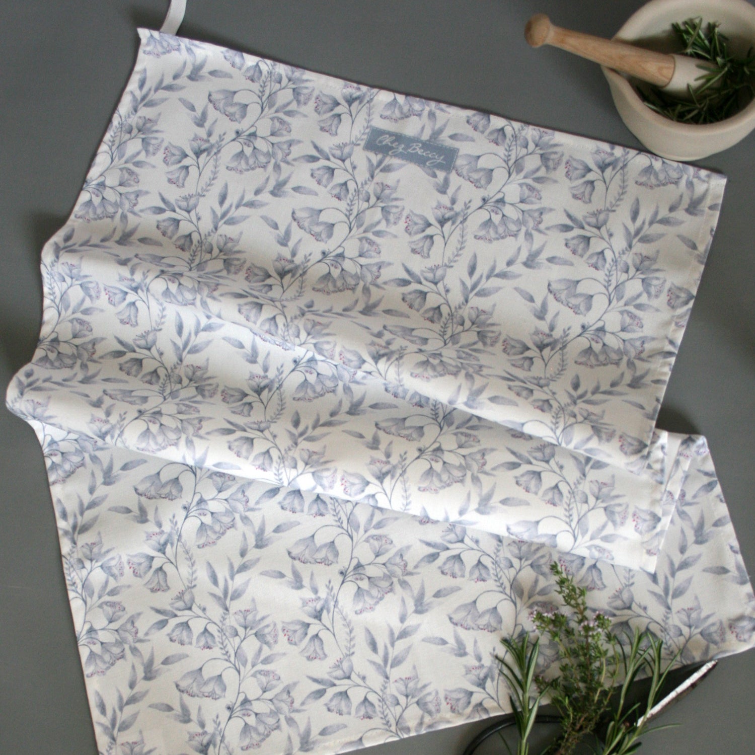 Grey Damask Floral Tea Towel on a grey background with cooking props
