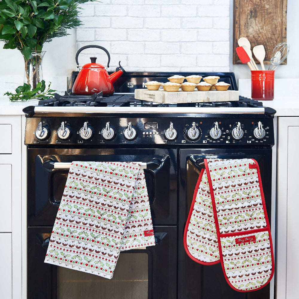 Christmas tea towel and oven glove with Christmas puddings, holly and hearts on a black range cooker