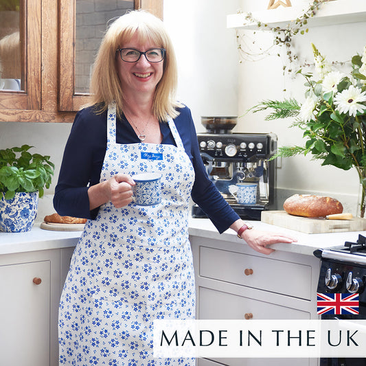Beccy standing in a kitchen holding a cup of tea wearing a blue ditsy floral apron