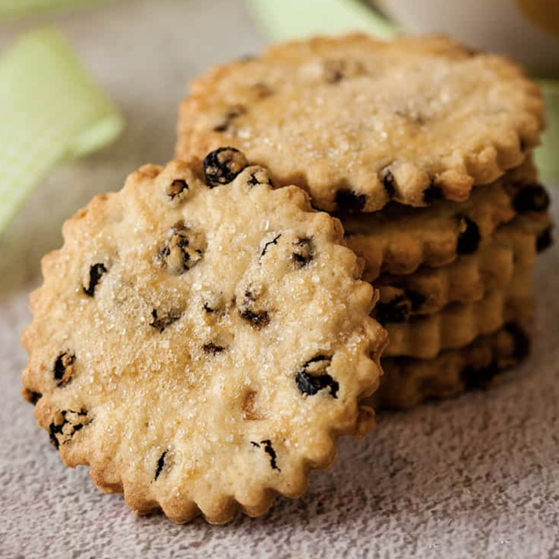 A close-up of golden, Easter biscuits with currants, sprinkled with sugar and stacked in a neat pile on a textured surface.