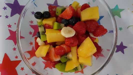 Summer fruit salad in a clear bowl with a rainbow stars tea towel