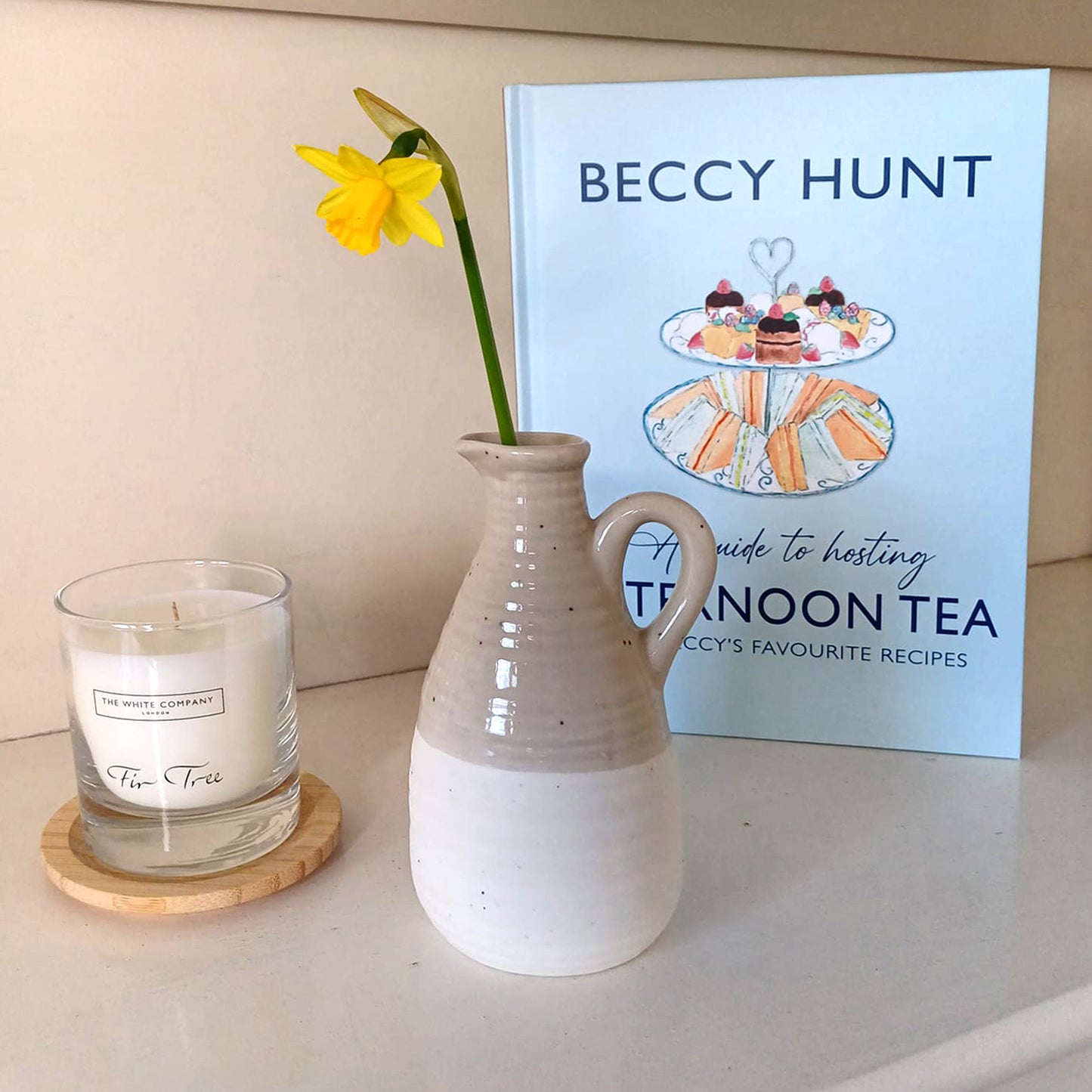 Book: 'A Guide to Hosting Afternoon Tea' by Beccy Hunt, featuring a pastel blue cover with an illustrated tiered cake stand, sandwiches, and sweet treats- displayed on a bookshelf. A must-have cookbook for afternoon tea lovers, featuring British-inspired recipes and hosting tips.