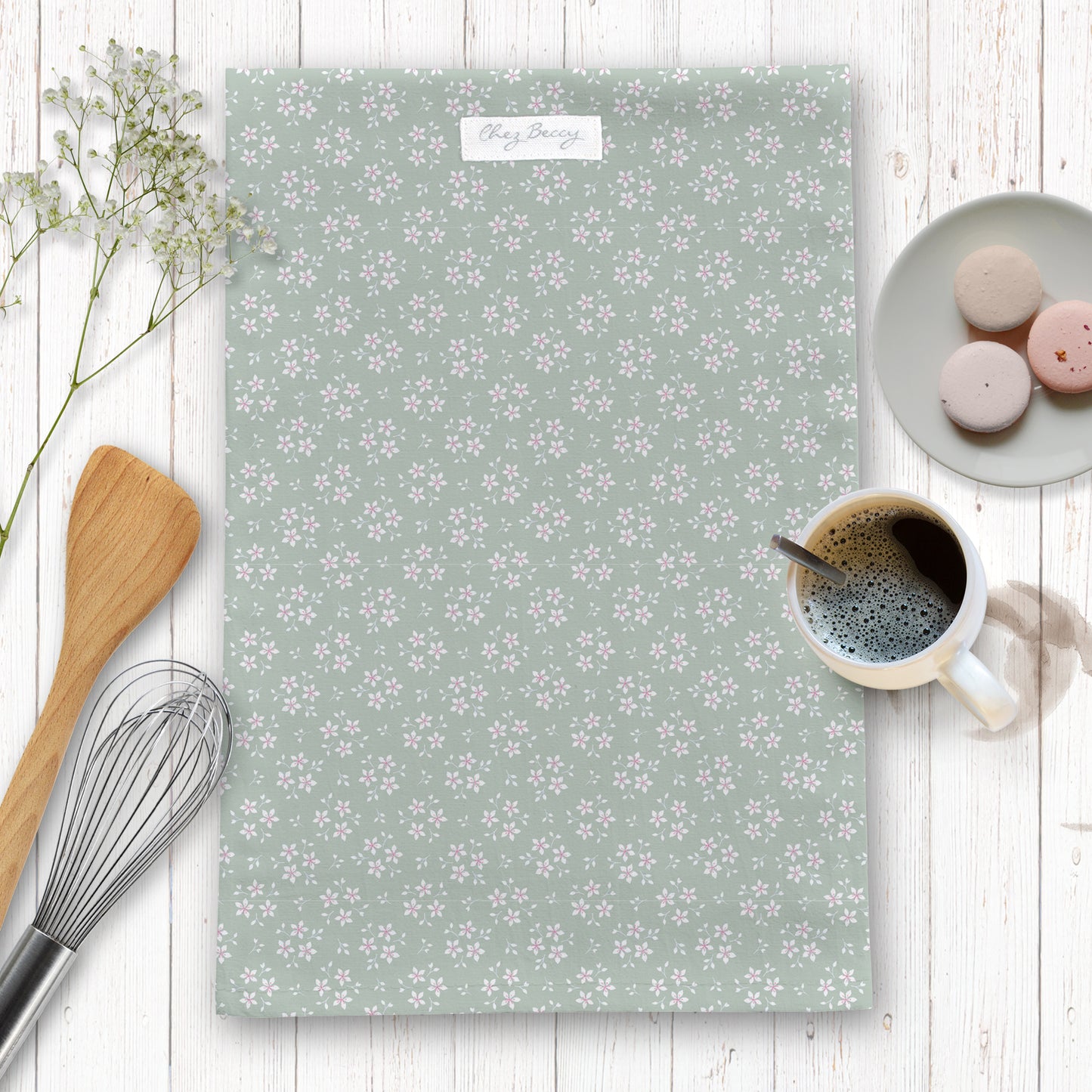 Sage green tea towel with little white flowers on a wooden background with baking props