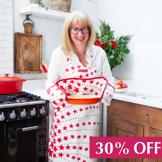 Woman in a red star apron holding a dish with red star double oven glove in a kitchen