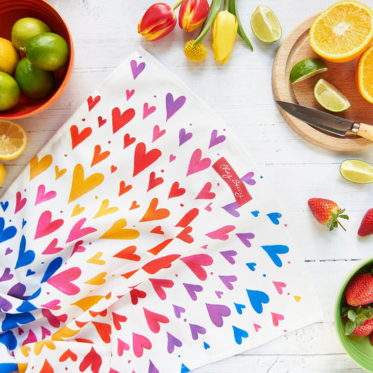 A 100% cotton tea towel featuring a vibrant spray of multicoloured hearts, adding a cheerful touch to any kitchen. Measuring approximately 70cm x 47cm, it's both absorbent and stylish. Designed and made in the UK.